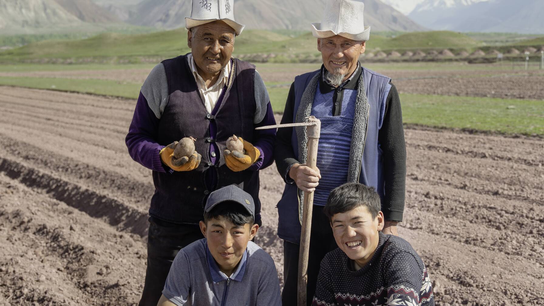 Avec son voisin et les deux fils du voisin, Shokirjon Shamirov plante des pommes de terre sur les parcelles tests de Caritas Suisse.