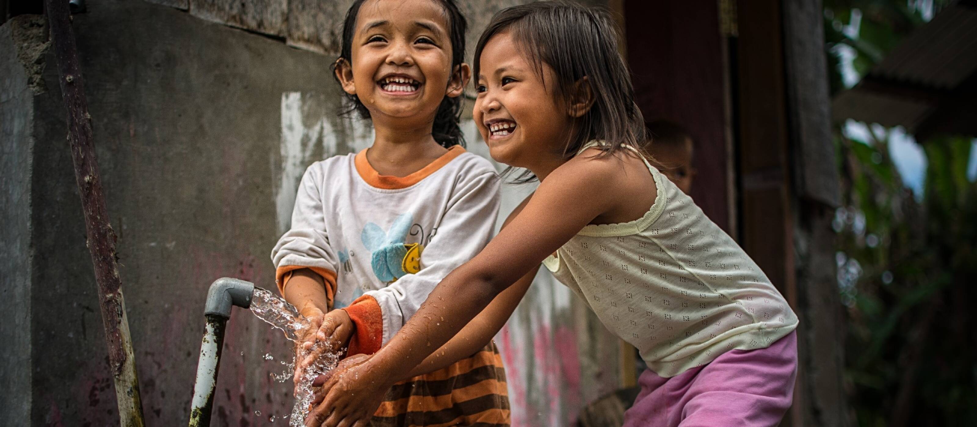 Two children laugh as they wash their hands in the village of Anca in Indonesia. 