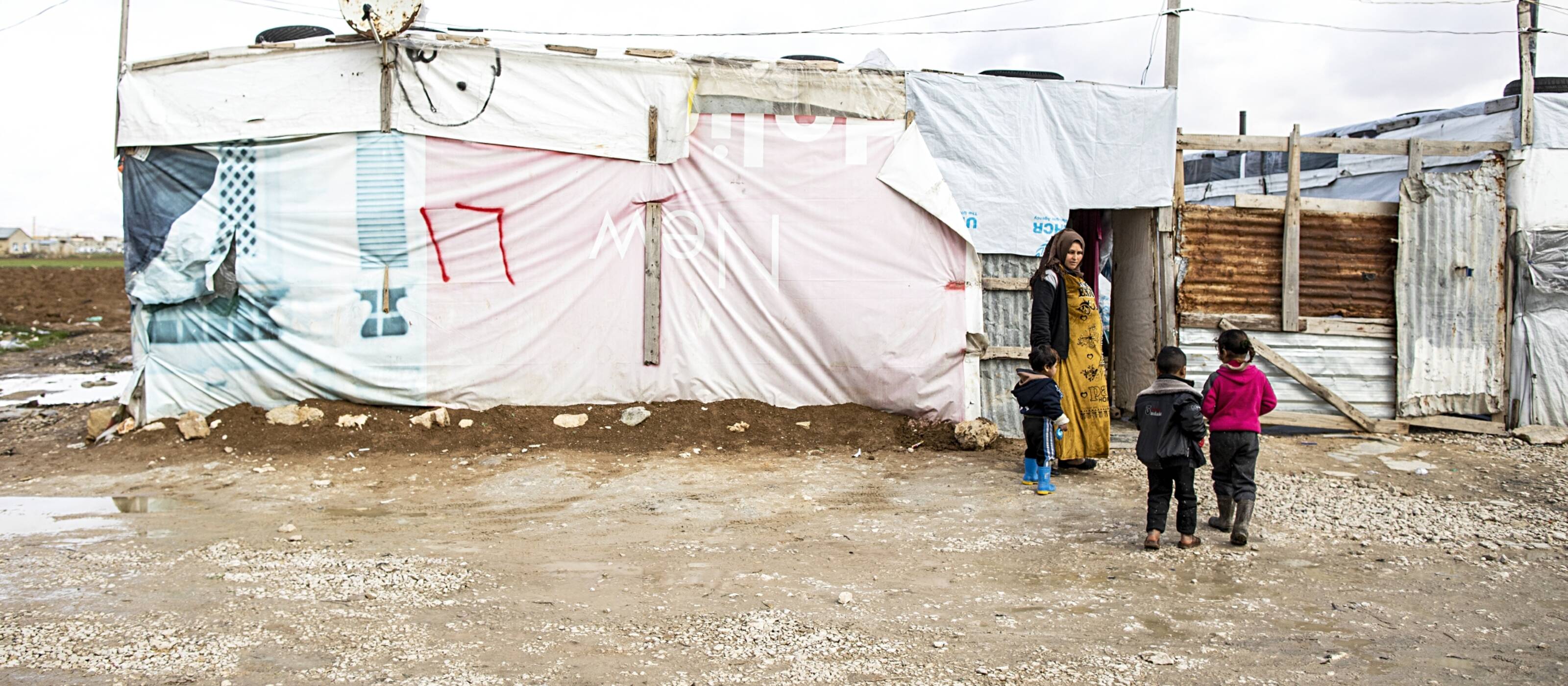 Eine Mutter steht mit ihren drei Kindern vor dem Eingang ihrer Unterkunft in einem Flüchtlingslager im Libanon.