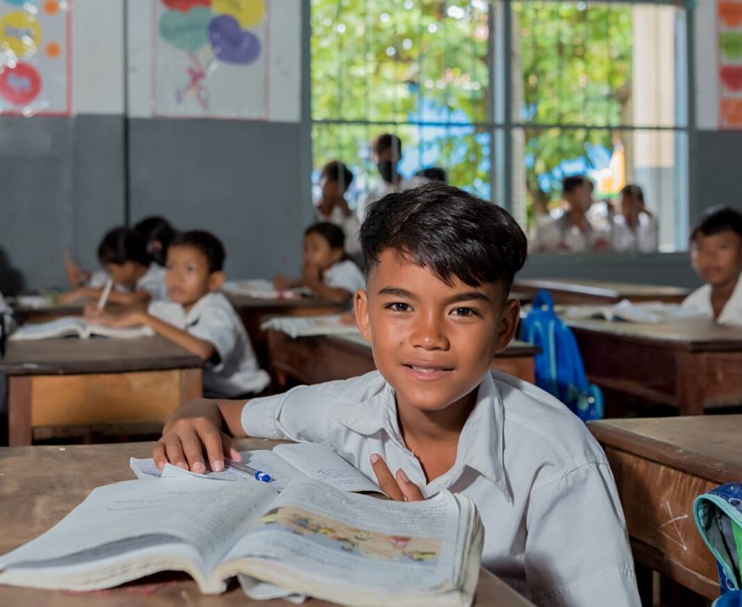 Ein Kind schaut inmitten seiner Klasse von seinen Schulbüchern auf und direkt in die Kamera.