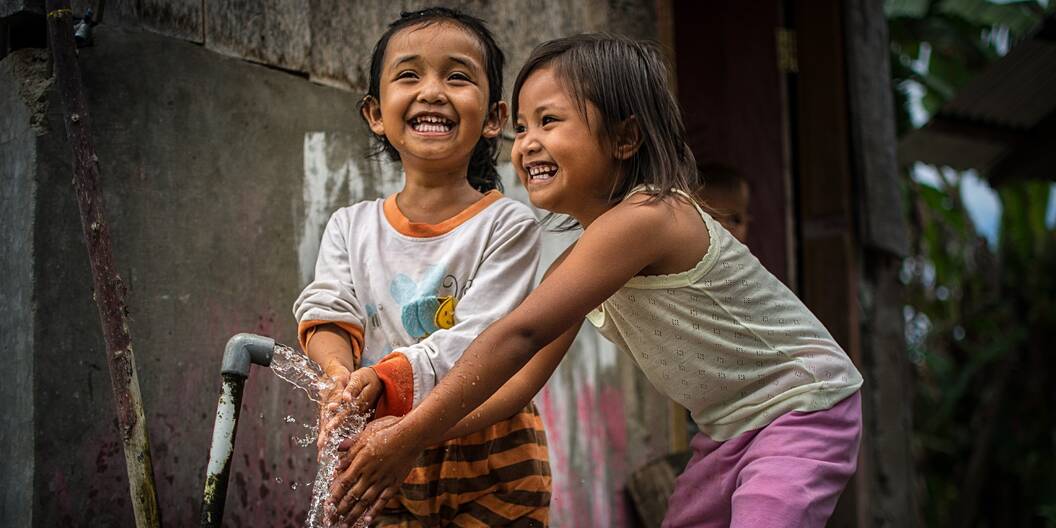 Zwei Kinder waschen sich lachend die Hände im Dorf Anca in Indonesien.