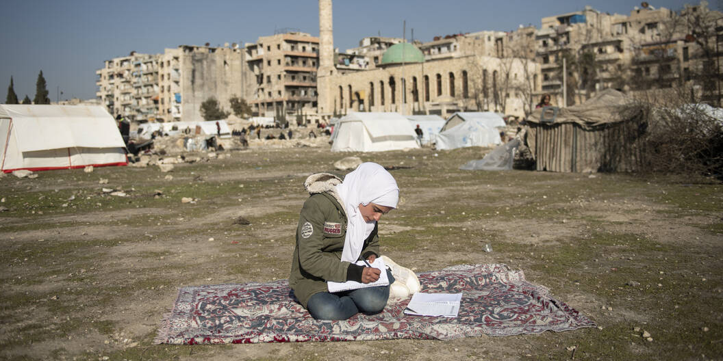 Ein syrisches Mädchen macht seine Hausaufgaben vor den Trümmern der Stadt Aleppo, die im Februar 2024 stark vom Erdbeben getroffen wurde.